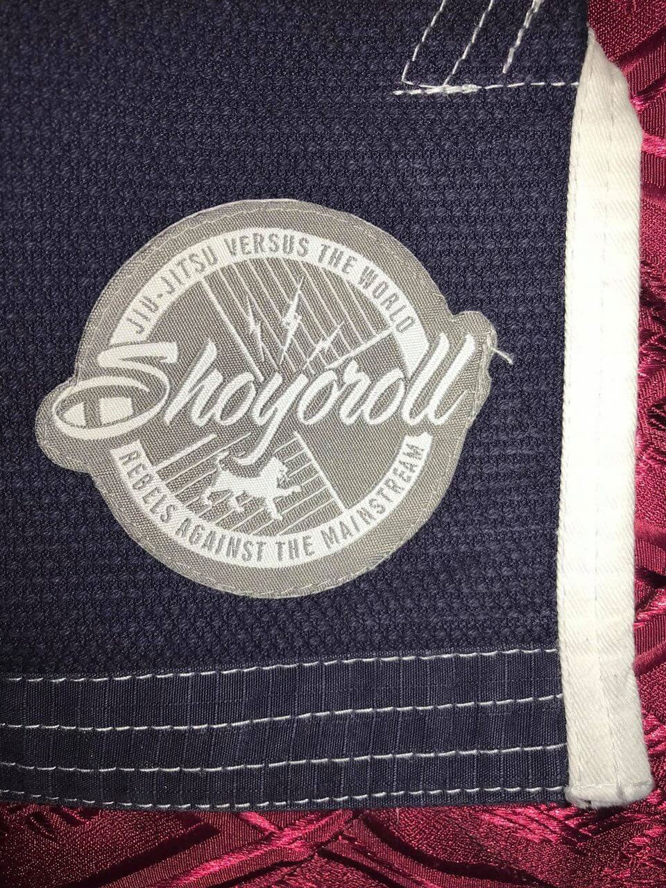 Shoyoroll Batch #8: The Yank, a navy blue Jiu-Jitsu gi featuring a lightweight 450 GSM pearl weave jacket and 12 oz ripstop cotton pants, part of the East vs. West series inspired by baseball legend 'The Great Bambino.' Includes contrast stitching, a foam collar, stretchy drawstring, ID/iPod pocket, and custom inner taping.