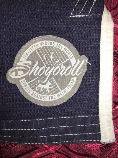 Shoyoroll Batch #8: The Yank, a navy blue Jiu-Jitsu gi featuring a lightweight 450 GSM pearl weave jacket and 12 oz ripstop cotton pants, part of the East vs. West series inspired by baseball legend 'The Great Bambino.' Includes contrast stitching, a foam collar, stretchy drawstring, ID/iPod pocket, and custom inner taping.