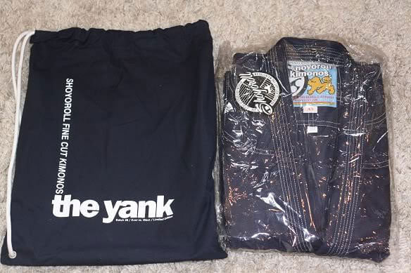 Shoyoroll Batch #8: The Yank, a navy blue Jiu-Jitsu gi featuring a lightweight 450 GSM pearl weave jacket and 12 oz ripstop cotton pants, part of the East vs. West series inspired by baseball legend 'The Great Bambino.' Includes contrast stitching, a foam collar, stretchy drawstring, ID/iPod pocket, and custom inner taping.