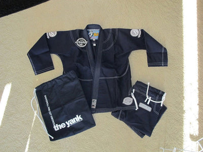 Shoyoroll Batch #8: The Yank, a navy blue Jiu-Jitsu gi featuring a lightweight 450 GSM pearl weave jacket and 12 oz ripstop cotton pants, part of the East vs. West series inspired by baseball legend 'The Great Bambino.' Includes contrast stitching, a foam collar, stretchy drawstring, ID/iPod pocket, and custom inner taping.