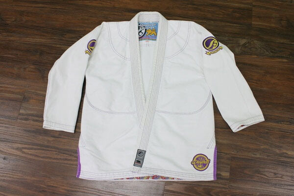 Shoyoroll Batch #8 White Mamba Gi, featuring a lightweight 450 GSM pearl weave jacket and 12 oz ripstop pants. Designed by artist John Smalls, this gi showcases a white base with purple trim. Released as part of the East vs. West Series on December 22, 2010, at 3:00 PM PST.