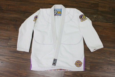 Shoyoroll Batch #8 White Mamba Gi, featuring a lightweight 450 GSM pearl weave jacket and 12 oz ripstop pants. Designed by artist John Smalls, this gi showcases a white base with purple trim. Released as part of the East vs. West Series on December 22, 2010, at 3:00 PM PST.